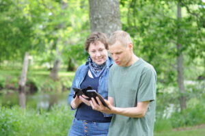 En kvinna och en man spelar GoGlad. De promeneras på en stig vid en å.