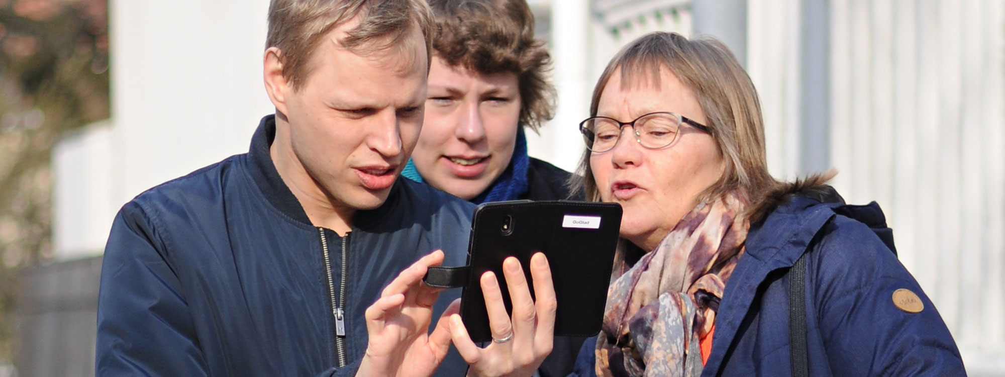 en man och två kvinnor är utomhus. De tittar på en smartphone.